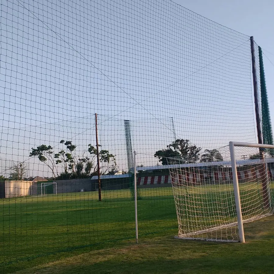 Campo de futebol com rede de proteção alta atrás do gol